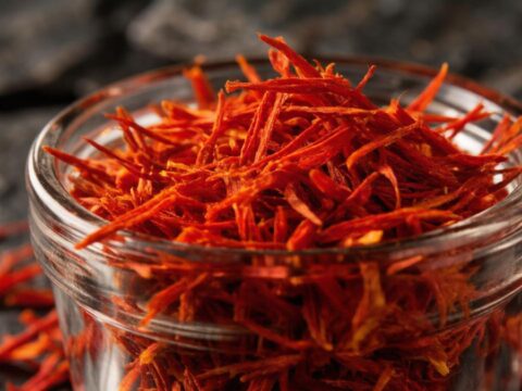 Нити настоящего красного шафрана в стеклянной чаше на темном фоне.