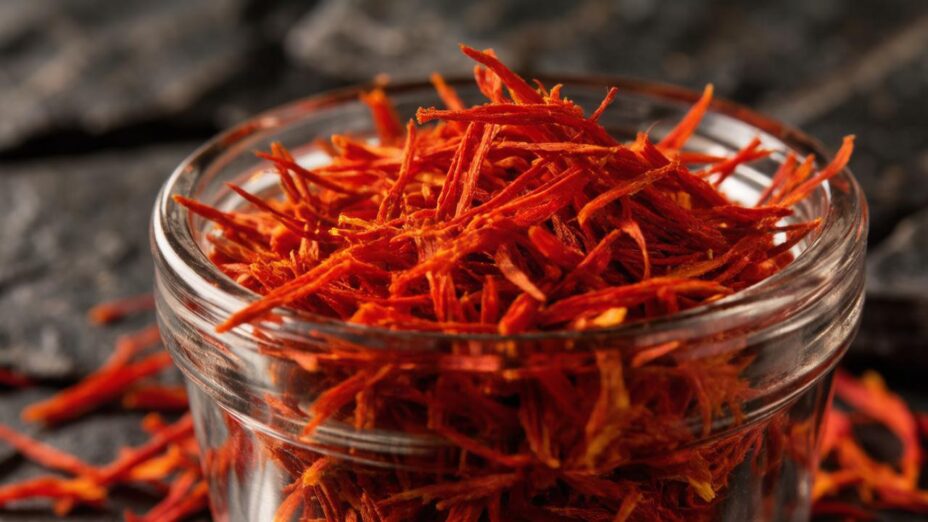 Нити настоящего красного шафрана в стеклянной чаше на темном фоне.